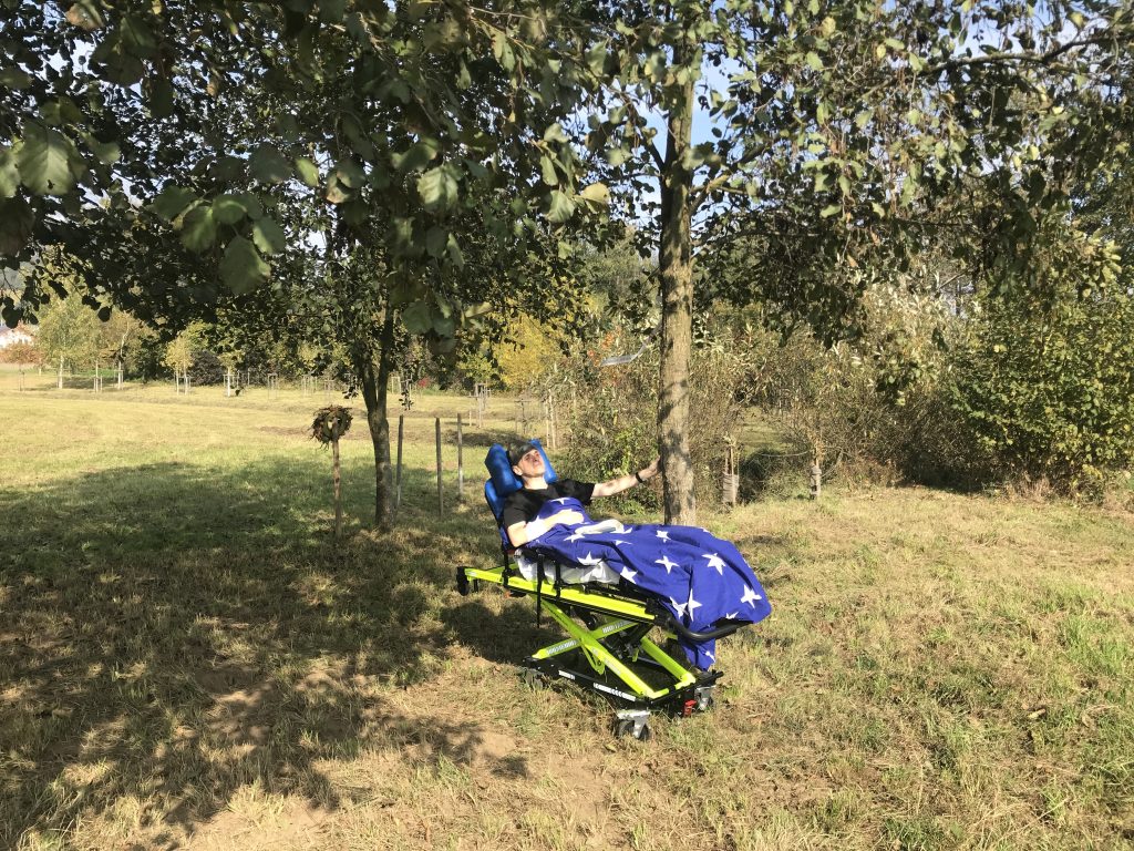 Martin liegend auf der Rettungstrage berührt er mit seiner Hand den Baum, bei dem er bald begraben wird.