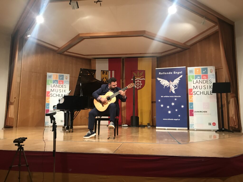 Mann mit Gitarre sitzt auf Bühne und spielt